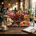 Personalized TrioAuraDesign MacBook case featuring a Stone Bouquet design with blush pink, burgundy, ivory and warm golden stone-effect flowers, deep green leaves and the custom name Angelina. The MacBook is displayed upright on a rustic wooden café table beside a cappuccino, open notebook, pen and small flower vases, with warm pendant lights and a softly blurred café interior in the background.
