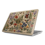 A focused side profile view of a silver MacBook featuring a custom hard shell case with a realistic 3D embroidery visual effect. The intricate design depicts a lush wildflower garden, a buzzing bumblebee, a Monarch butterfly, and a humming bird on a textured light beige surface.