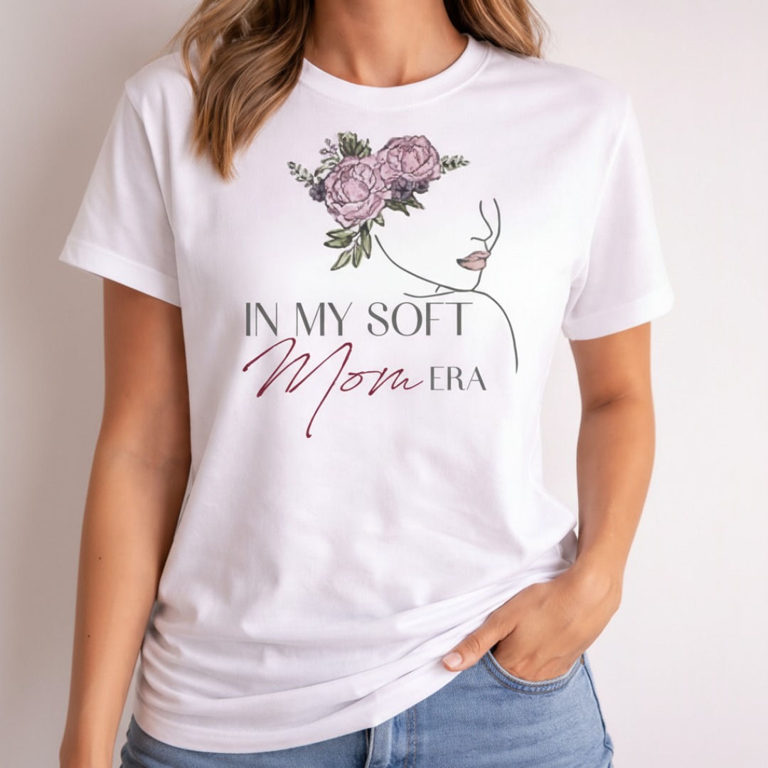 Stylish portrait of a woman wearing a white "In My Soft Mom Era" T-shirt, showing the elegant line art and floral design in a studio setting.