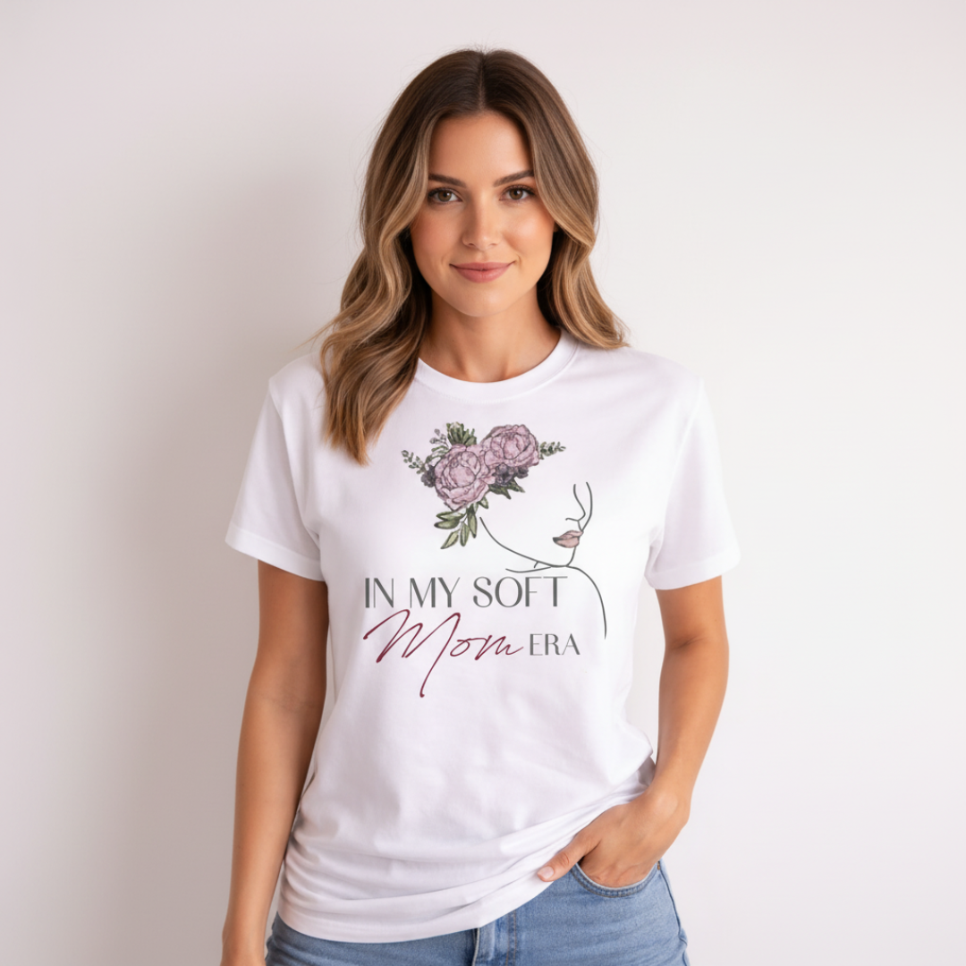 Close-up of a smiling young woman wearing a white "In My Soft Mom Era" T-shirt, highlighting the minimalist line art of a woman's profile with a pink peony bouquet header.