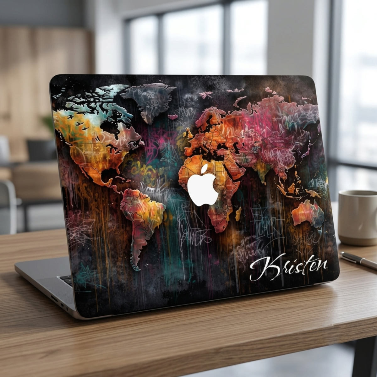 Front lifestyle photo of a personalized artistic world map MacBook case by TrioAuraDesign displayed on a partially open laptop. The hard-shell case features a colorful abstract world map with vibrant watercolor textures, dark wood background details, and the personalized name "Kristen" in elegant white script. The image highlights the smooth protective finish, slim lightweight profile, unique travel-inspired artwork, and precise fit for MacBook Air and MacBook Pro models.