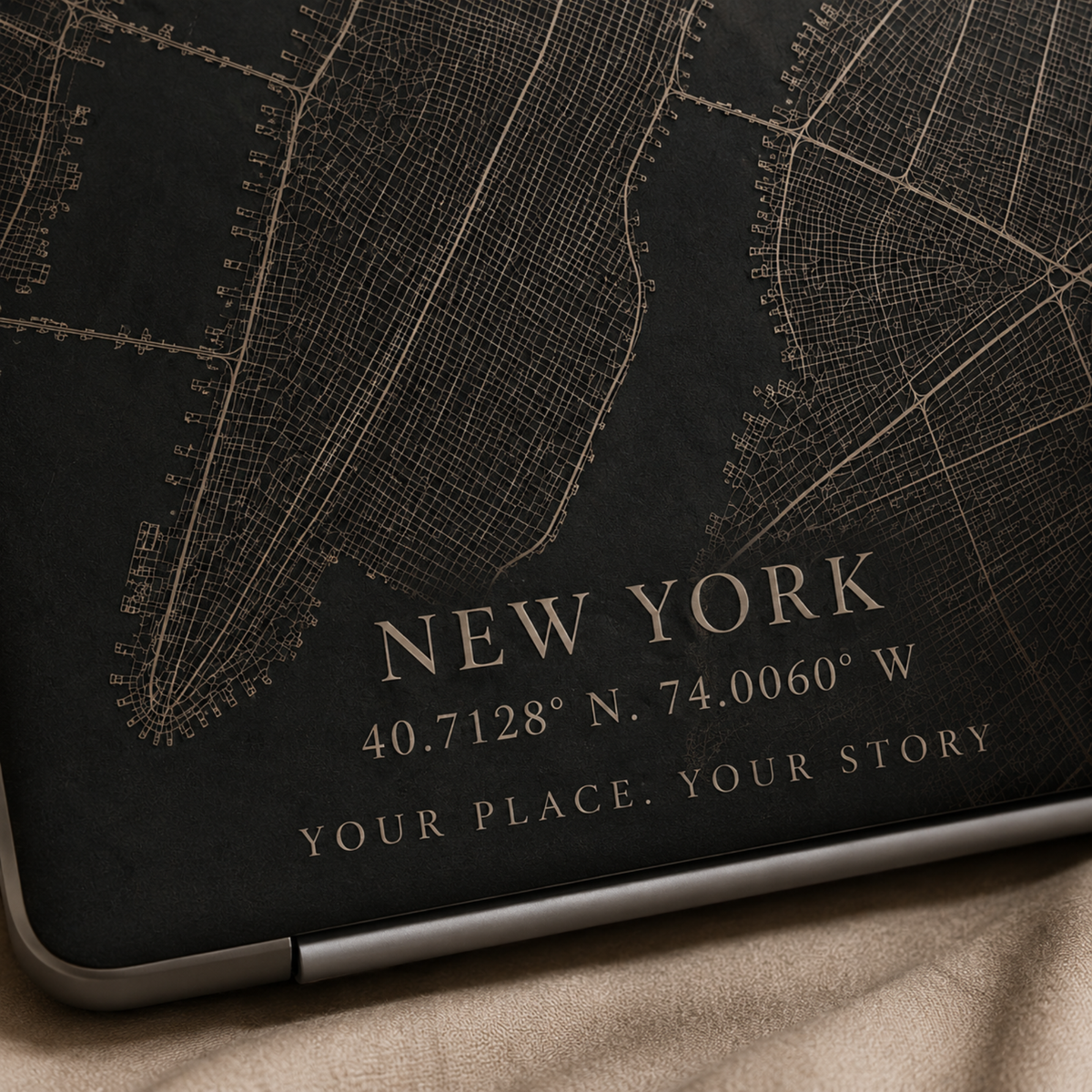 Close-up of a personalized City Map MacBook case from TrioAuraDesign, featuring a dark New York street map with custom city text “NEW YORK,” coordinates, and the phrase “YOUR PLACE. YOUR STORY.” The detailed map lines and warm beige lettering are shown up close on the smooth printed hard shell, highlighting the custom map design and personalization details.