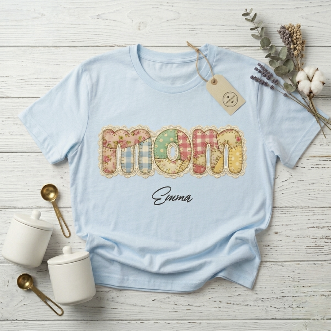 Smiling young woman posing outdoors in a light blue personalized "Mom" T-shirt, showcasing the cozy grandmillennial quilt aesthetic print.
