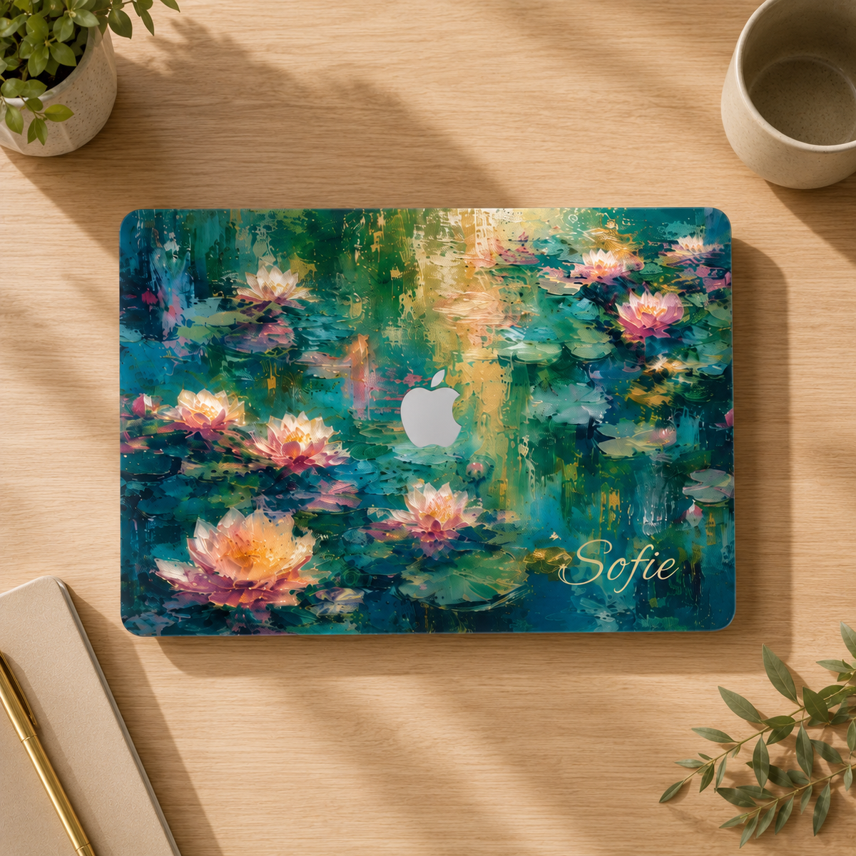 Top view of a MacBook in a water lilies hard shell case personalized with Sofie, on a wooden desk.