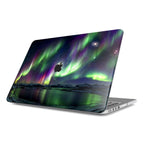 Isolated angled view of a MacBook with a protective hard shell case against a white background. The case features a Northern Lights design of a vibrant green and purple Aurora Borealis over a snowy arctic landscape and a reflective lake, with a dark cutout showing the Apple logo.
