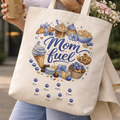 Smiling young woman posing outdoors, holding a personalized "Mom Fuel" canvas tote bag while enjoying a take-out coffee, showing the vibrant food illustration and custom script details.
