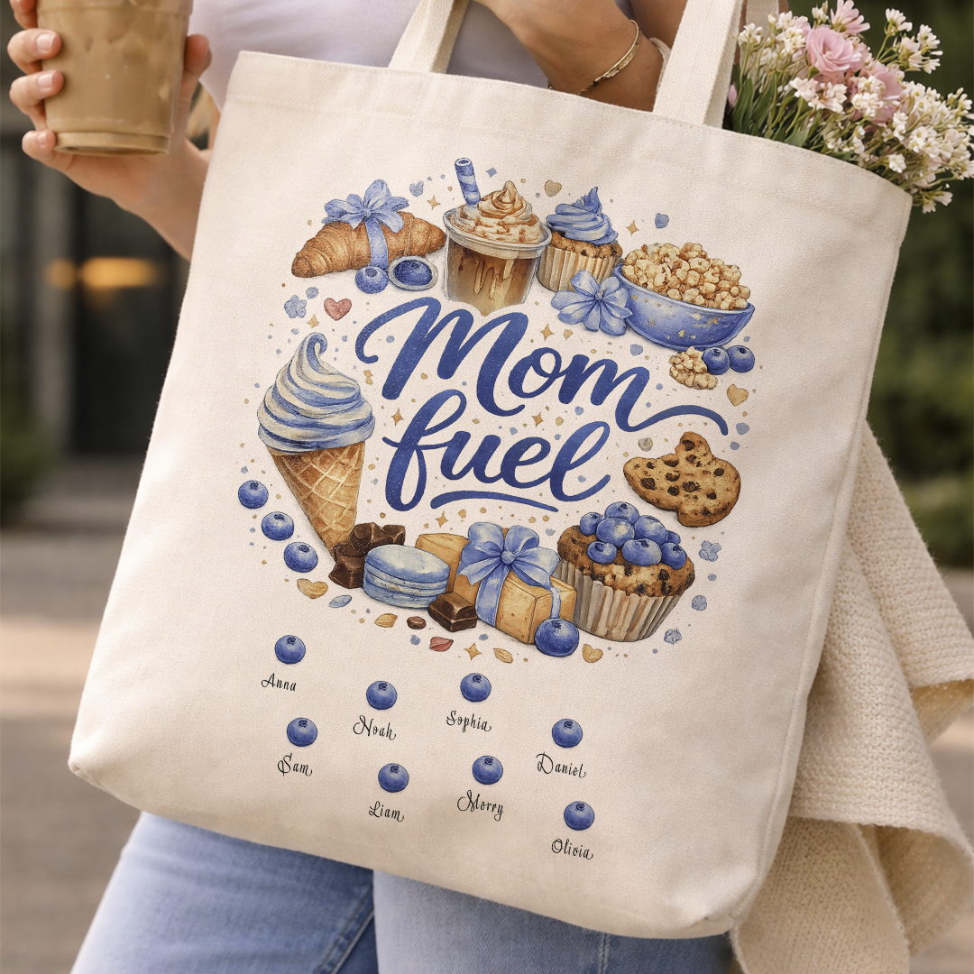 Smiling young woman posing outdoors, holding a personalized "Mom Fuel" canvas tote bag while enjoying a take-out coffee, showing the vibrant food illustration and custom script details.
