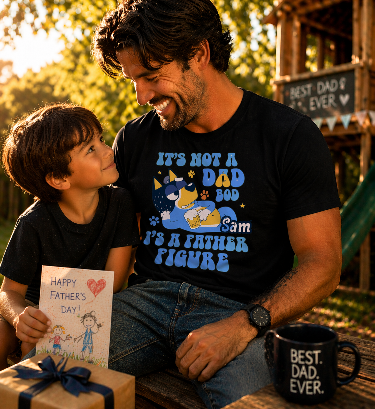 A smiling father in a black personalized t-shirt with a "Father Figure" cartoon dog and the name "Sam," sitting with his son holding a Father's Day card.