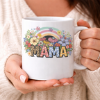  Woman holding a custom MAMA ceramic mug with a vibrant boho wildflower and rainbow graphic, perfect for a cozy morning
