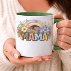 Woman holding a custom MAMA ceramic mug with a vibrant boho wildflower and rainbow graphic, perfect for a cozy morning
