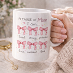 Because of Mom I Am..." inspirational mug with pink bows illustration and text listing qualities: loved, strong, brave, confident, kind. Special Mother's Day present.