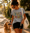 Lifestyle photo of a smiling woman walking her Golden Retriever on a leash, wearing a personalized heather grey 'Best Dog Mom' T-shirt with multi-colored leopard print letters and the custom name 'Georgia', and carrying a canvas tote bag.