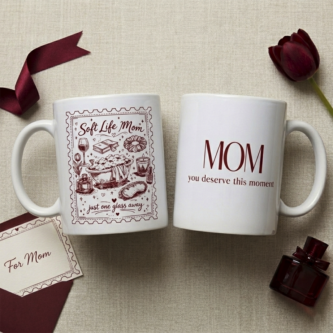 White ceramic mug showing two sides: one with a detailed burgundy illustration of a bathtub and "Soft Life Mom" text, the other with "MOM: you deserve this moment" in elegant typography. Mother's Day gift by TrioAuraDesign.