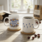 Close-up of the "Mom Fuel" mug design showing detailed watercolor croissants, cupcakes, and blueberries with the name Noah scripted below.
