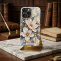 iPhone in a Blue Bloom magnolia stained glass effect case personalized with ADALINDA, on a gold stand on marble with old books. Printed effect, smooth glossy finish.