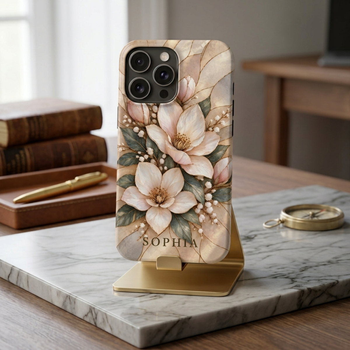iPhone in a Champagne Bloom magnolia printed stained glass effect case personalized with SOPHIA, on a gold stand.