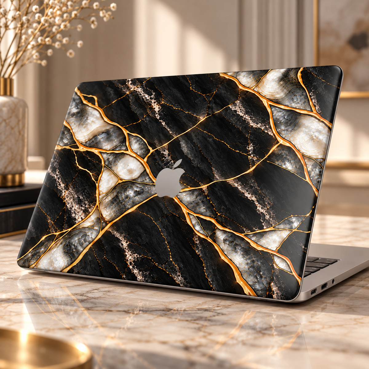 MacBook in a Black Pearl marble printed case with gold veins and pearly inlay, Apple logo visible, on a marble table in warm light.