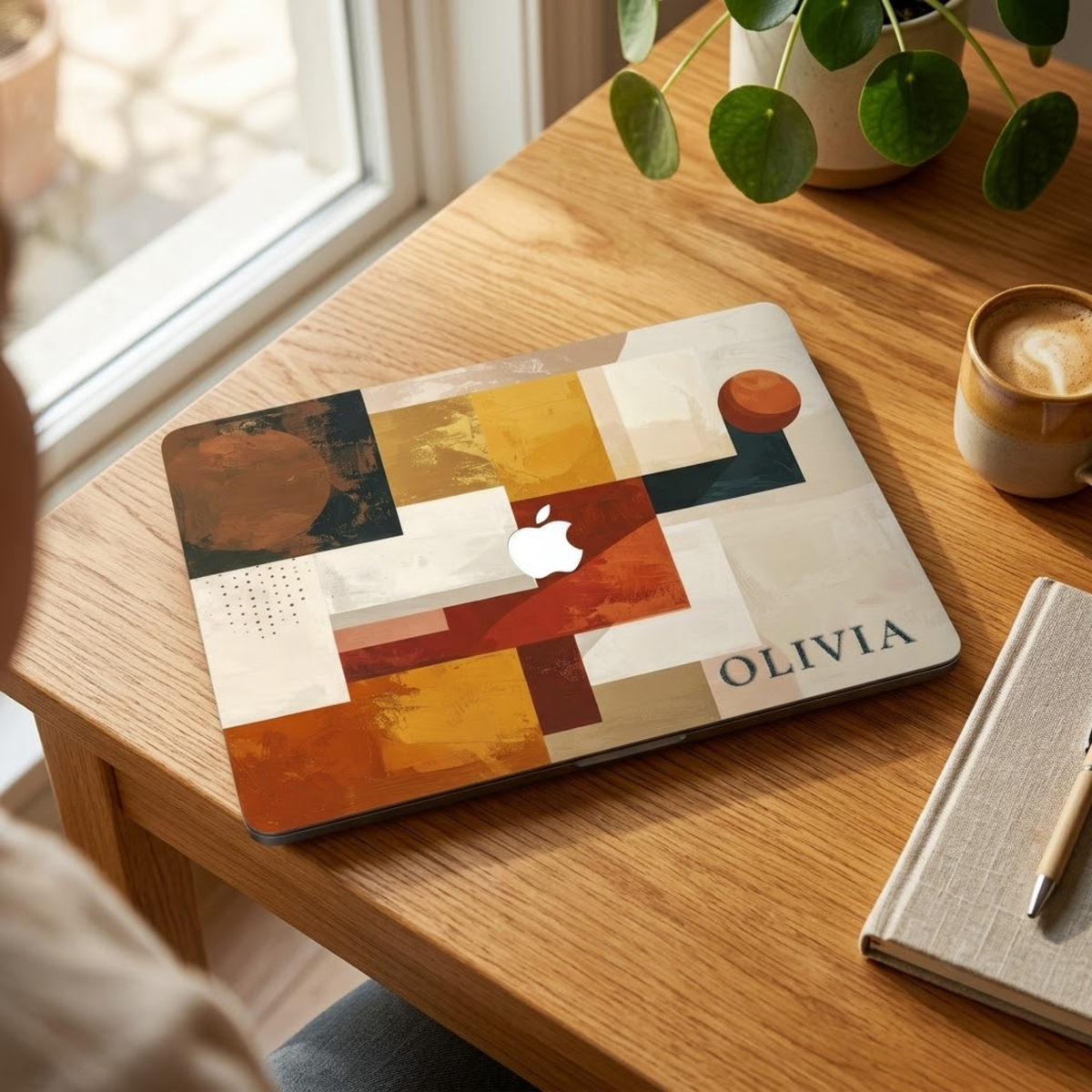 Personalized abstract geometric MacBook case with custom name Olivia in terracotta mustard navy and cream color blocks, displayed on wooden desk near sunny window with coffee cup, potted plant and linen notebook — bold architectural collage hard shell laptop cover with elegant serif name personalization, Apple logo visible through an unprinted area, slim snap-on fit, for MacBook Air 13 M2 M3 M4 M5 and MacBook Pro 14 16 M3 M4 M5, modern aesthetic personalized gift for creative professionals