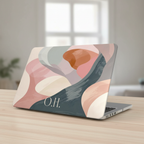A MacBook with a personalized neutral abstract case in soft pink, sage green, and beige on a wooden desk with a window view, featuring the monogram O.H.