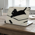 A MacBook with a protective hard shell case featuring a minimalist black ink sketch of a cat lying on an open book, set against a matte cream-colored background. The laptop is placed on a wooden desk in a cozy office environment with coffee mugs and notebooks, showcasing the aesthetic and artistic design of the cover.