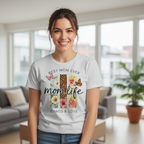 A smiling young woman wearing a grey Heather "Best Mom Ever" t-shirt, showcasing the unique multi-panel floral leopard and butterfly graphic design in an outdoor park setting.