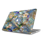 Isolated angled view of a MacBook with a protective hard shell case against a white background. The case features an intricate stained glass mosaic design of emerald green hummingbirds and lilies with gold-accented outlines. A central cutout in the artistic pattern reveals the Apple logo on the silver laptop lid.
