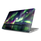 Angled view of a MacBook featuring a premium hard shell case with a vibrant Northern Lights design. The celestial artwork displays emerald green and deep purple Aurora Borealis dancing across a starry night sky over a reflective arctic lake and snow-capped mountains.