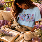 Lifestyle shot of a woman in a light blue personalized 'Cat Mum' T-shirt with purple floral lettering, cuddling her cat in a sunlit garden setting with a 'Fueled by Love & Purrs' mug.