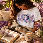 Lifestyle shot of a woman in a white  personalized 'Cat Mum' T-shirt with purple floral lettering, cuddling her cat in a sunlit garden setting with a 'Fueled by Love & Purrs' mug.