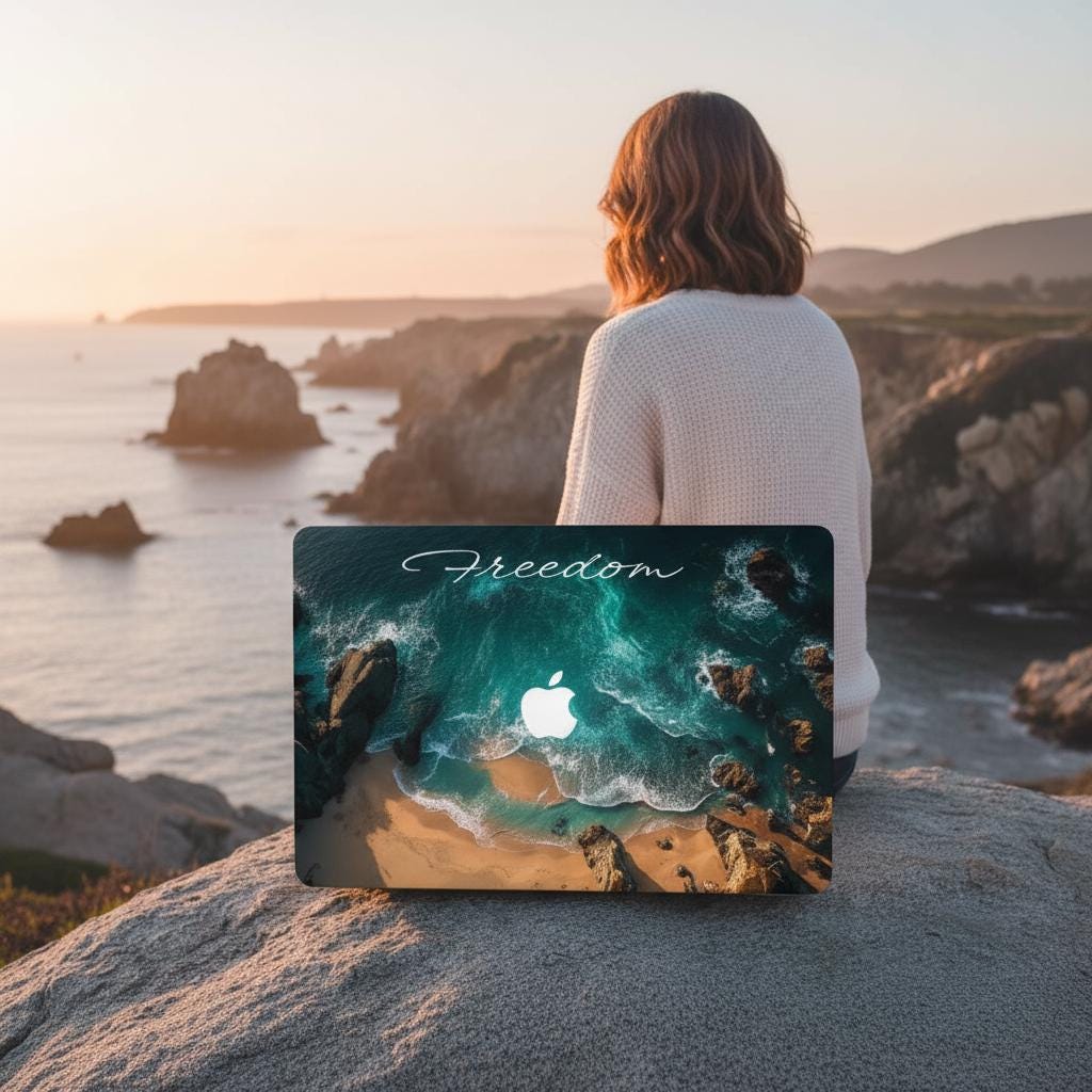 Woman sitting on coastal rocks at sunset holding MacBook with custom ocean aerial photography case, Freedom personalized laptop cover
