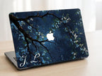 Custom initial MacBook case with dark navy botanical floral design, flowering branches on deep blue background, personalized with white script initials J.L., lifestyle photo on wooden desk