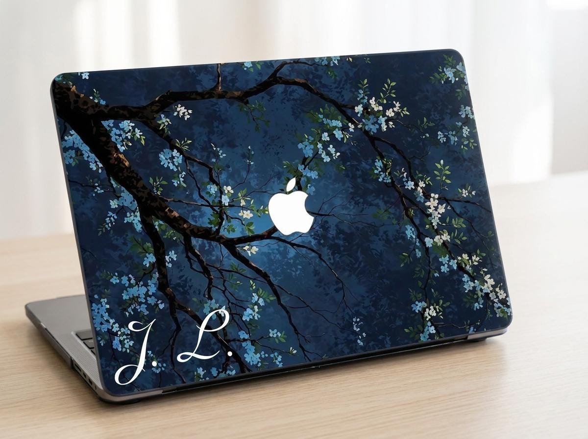 Custom initial MacBook case with dark navy botanical floral design, flowering branches on deep blue background, personalized with white script initials J.L., lifestyle photo on wooden desk
