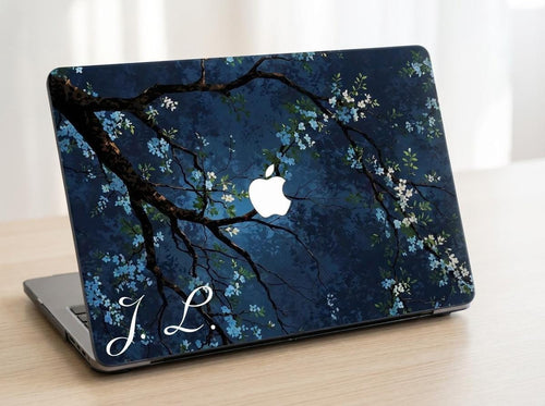 Custom initial MacBook case with dark navy botanical floral design, flowering branches on deep blue background, personalized with white script initials J.L., lifestyle photo on wooden desk