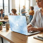 Custom name MacBook case with soft blue watercolor sky and cloud print, personalized with white signature script, lifestyle photo of woman working in modern office coworking space