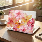 Custom watercolor hibiscus MacBook case with personalized name in serif script, pink coral floral laptop cover, warm desk lifestyle setup with coffee and sunlight