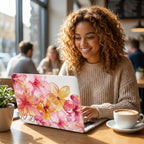 Smiling woman working on MacBook with custom watercolor hibiscus case and personalized name, pink floral laptop cover, cozy cafe with coffee