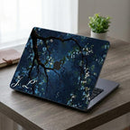 Custom initial MacBook case with dark navy botanical floral design, personalized with white script initials J.L., side angle view on wooden desk with plants and natural light