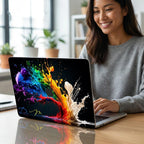Woman smiling while working on MacBook with colorful paint splash case, personalized initials on abstract rainbow laptop cover, bright office with plants