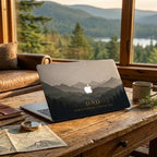 Personalized dark mountain landscape MacBook case with custom text DAD and date on rustic wooden desk with compass, map and coffee — moody forest silhouette hard shell laptop cover with misty grey gradient mountains, gold personalized inscription, Apple logo cutout, slim snap-on fit, for MacBook Air 13 M2 M3 M4 M5 and MacBook Pro 14 16 M3 M4 M5, personalized Father's Day gift for dad, adventure nature aesthetic laptop accessory