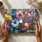 Hands holding the personalized Colorful Garden MacBook case on a marble surface with pampas grass and a ceramic cup. Stained glass look is printed, not real glass.