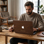 Man working on a personalized wood grain MacBook case with custom name David and phrase "Focused. Driven. Building my legacy." Rich warm walnut wood texture hard shell case displayed in a cozy home office with bookshelf, wooden desk and natural light. Hard shell cover for MacBook Air 13 M3 M4, MacBook Air 15, MacBook Pro 14 M5 2026, MacBook Pro 16. Perfect personalized birthday gift or graduation gift for him, husband or boyfriend.