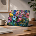 Colorful Garden floral MacBook case with Georgia in gold lettering on a home office desk with a mug, gold pen and potted plant.