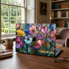 MacBook in the Colorful Garden stained glass effect case on a dark wooden desk in a home library with bookshelves and a gold lamp.