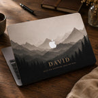 Personalized mountain landscape MacBook case by TrioAura Design displayed on a wooden desk with coffee and notebook. Custom name laptop cover for MacBook Air and MacBook Pro in a warm cozy workspace.