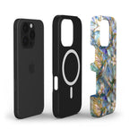 Exploded view of a MagSafe-compatible stained glass effect iPhone case showing the phone, shock-absorbing TPU inner liner, and printed polycarbonate outer shell. The glossy outer case features vibrant hummingbirds, white lilies, and botanical artwork inspired by stained glass in blue, teal, ivory, and gold tones. The image highlights the dual-layer protective construction, precise cutouts, and premium edge-to-edge UV printing. Available from TrioAuraDesign.