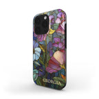 Angled product view of a personalized iPhone case with the custom name Georgia, featuring a colorful stained glass effect with layered pink, purple, blue, green and yellow botanical artwork and intricate golden-looking printed outlines. The clean white background highlights the full-wrap print, slim profile, rounded edges and protective camera area. The stained glass appearance is a printed visual effect on a smooth glossy Tough or MagSafe Tough case from TrioAuraDesign.