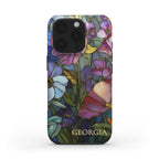Front product view of a personalized iPhone case with the custom name Georgia, featuring a colorful stained glass effect with layered pink, purple, blue, green and yellow botanical artwork and intricate golden-looking printed outlines. The clean white background clearly highlights the full design, personalization, rounded edges and protective camera area. The stained glass appearance is a printed visual effect on a smooth glossy Tough or MagSafe Tough case from TrioAuraDesign.