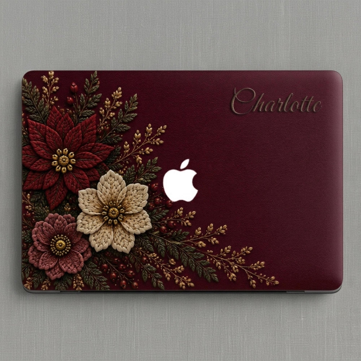 Personalized deep wine Crochet effect floral MacBook case from TrioAuraDesign, shown in a clean top-down product view. The smooth hard shell features rich burgundy, ivory and dusty rose flowers with botanical greenery, berries and gold-toned details, custom name “Charlotte” at the upper right, and a centered Apple logo. Elegant dark floral laptop cover for MacBook Air, Pro and Neo models, available in my shop.