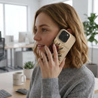 Personalized ivory embroidery effect floral iPhone case from TrioAuraDesign, shown in use during a phone call in a bright office setting. The smooth printed case features deep burgundy, ivory and dusty rose flowers with botanical greenery, berries and gold-toned details, plus the custom name “Charlotte” near the camera area. Elegant personalized floral phone case with a realistic embroidered look and smooth finish, available in my shop.