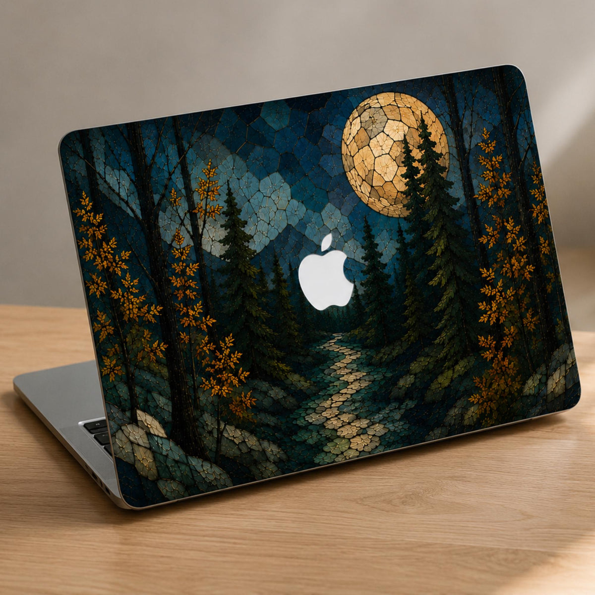 Open MacBook shown at an angle on a wooden desk with a stained glass effect hard shell case featuring a dark evergreen forest, golden autumn leaves, blue mountain layers, winding path and large glowing full moon. The Apple logo is visible in the center of the forest design. Custom personalized laptop cover compatible with MacBook Air 13 15, MacBook Pro 13 14 16 and MacBook Neo. Nature-inspired fall case by TrioAuraDesign.